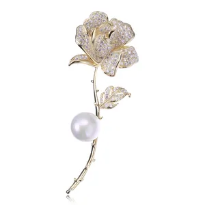 Dettaglio macro di una spilla a rosa dorata con petali di zirconi e una perla bianca