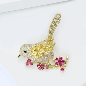 Détail de broche oiseau avec zircons colorés sur branche de fleur dorée, fond blanc
