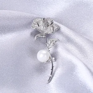 Dettaglio macro di spilla a rosa d'argento con zirconi e una perla bianca sulla seta
