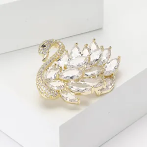 Elegante broche de cisne dorado con micropavé de circonitas sobre soporte geométrico blanco