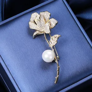 Dettaglio dell'elegante spilla a rosa dorata con petali in zircone e una grande perla bianca