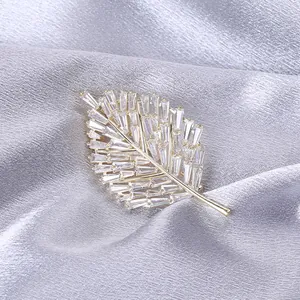 Macro della spilla a foglia dorata con pavé di zirconi su fondo di raso argentato