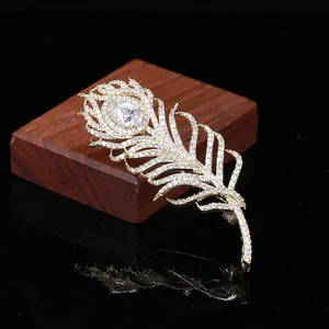 Détail macro d'une broche plume dorée avec pavé de zircons et cristal en goutte d'eau