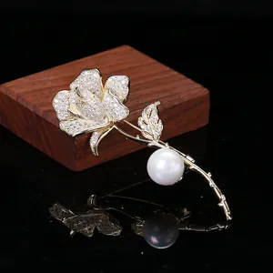 Macro di elegante spilla a rosa dorata con petali in zircone e una grande perla bianca