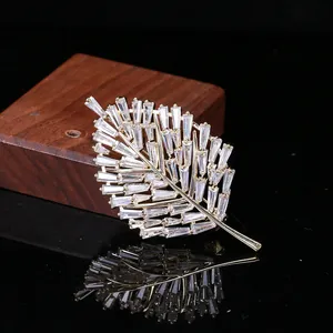 Elegante spilla a foglia dorata con zirconi taglio baguette su superficie a specchio