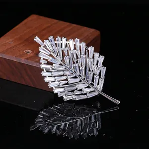 Dettaglio macro della spilla a foglia d'argento con zirconi riflessa sul legno