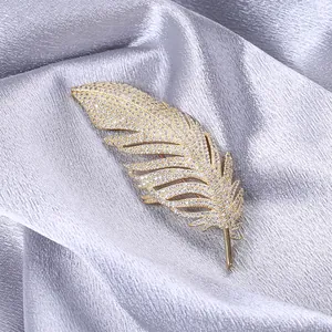 Detailed macro view of golden feather brooch with pavé zircon on silk fabric