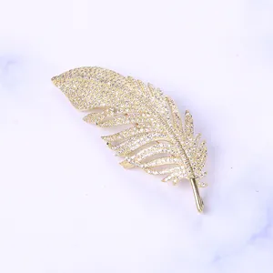 Macro view of feather brooch with gold plating and sparkling white zircons on marble