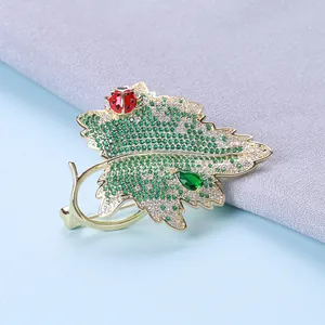Broche feuille dorée avec zircon vert et coccinelle sur fond textile doux