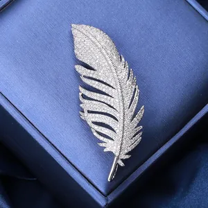 Macro detail of silver feather brooch with sparkling zircons on blue silk background