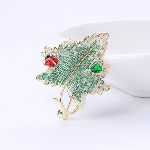 Détail macro d'une broche feuille dorée avec zircons verts et petite coccinelle rouge