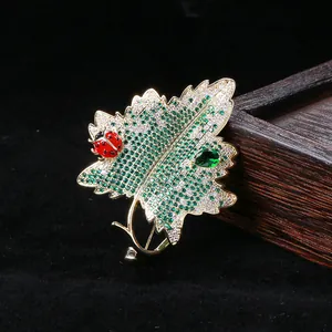 Broche feuille plaquée or avec zircons étincelants et coccinelle sur support en bois noir