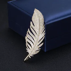 Close-up of elegant gold feather brooch with zircon pave settings on dark background