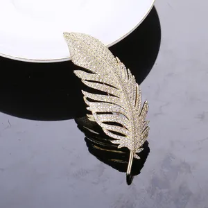 Macro detail of golden feather brooch with shimmering zircon inlay on dark background