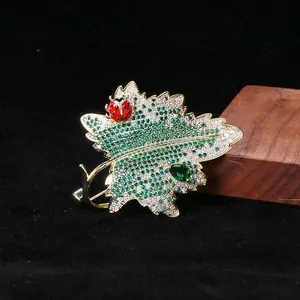 Détail macro d'une broche feuille dorée avec zircons verts et petite coccinelle rouge