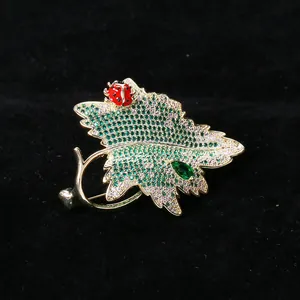 Détail macro de la broche feuille dorée sertie de zircons et d'une petite coccinelle