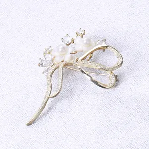 Detail einer goldenen Schleifenbrosche mit Muschelblumen, Strass und Perlen