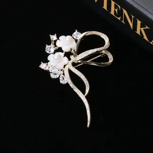 Eleganter goldener Schleifenbrosche mit weißen Muschelblumen, Perlen und Zirkonia auf Schwarz