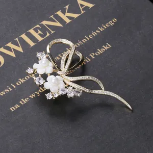 Detail einer vergoldeten Schleifenbrosche mit Muschelblumen und Zirkonia auf Box
