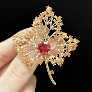 Macro detail of luxury maple leaf brooch featuring a red zircon and golden plating