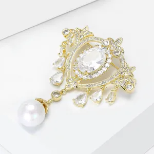 Close-up of golden baroque heart brooch with central crystal and white pearl drop