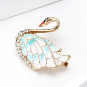 Elegant gold alloy swan brooch with white enamel wings and sparkling rhinestones for suits
