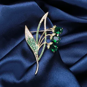 Detailed close-up of zircon campanula brooch with green stones on blue silk fabric