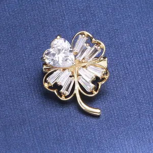 Macro detail of four-leaf clover brooch with sparkling heart-shaped zircon on blue fabric