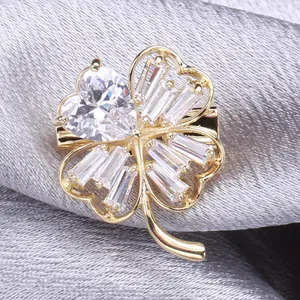 Macro detail of gold four-leaf clover brooch with sparkling heart-shaped zircon on silk fabric