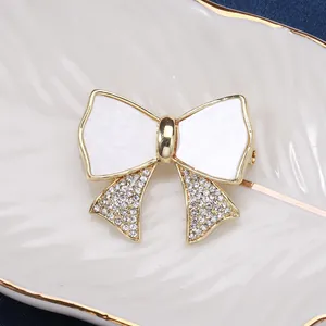 Elegant gold bow brooch with white enamel and sparkling rhinestones on a leaf tray
