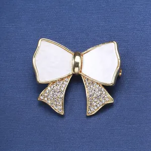 Elegant gold bow brooch with white enamel inlay and sparkling rhinestone accents