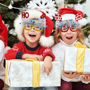 Children wearing festive Christmas glasses with tinsel and Santa motifs by a holiday tree