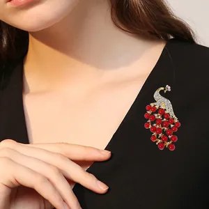 Eleganter Pfauen-Anstecker mit roten Perlen und Kristallen an einem dunklen Jackett