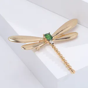 Elegant gold dragonfly brooch with green rectangular stone on a minimalist display stand