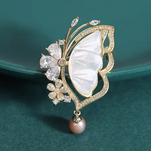 Elegant gold butterfly brooch with natural shell wings and purple pearl drop pendant