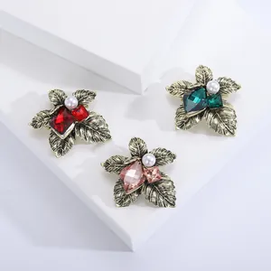Vintage leaf brooches with colorful gemstones and pearls on white display platforms
