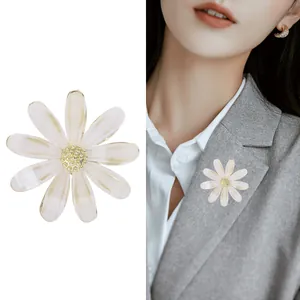 Broche fleur marguerite avec centre doré et pétales pailletés sur un blazer gris