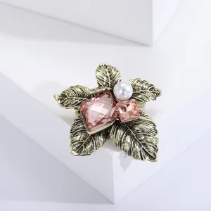 Vintage crystal flower brooch with bronze leaves and pink stones on a white pedestal