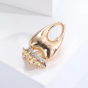Close-up of golden tooth-shaped brooch with crown decoration and small rhinestones