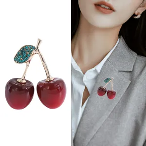 Détail d'une broche cerise rouge avec tige dorée et feuilles étincelantes sur un blazer