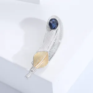 Détail d'une broche plume avec pierre bleue incrustée et finitions métal bicolores
