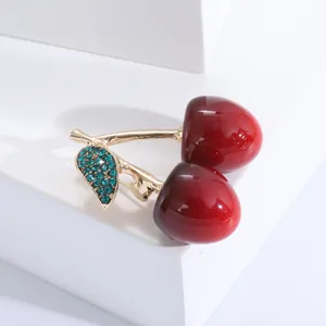 Vue macro d'une broche cerise en émail rouge avec base dorée et cristaux bleus fins