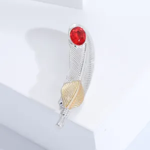Vue macro de la broche plume bicolore ornée d'une gemme rouge sur un socle épuré