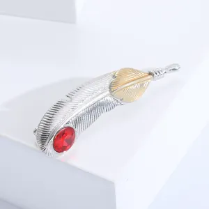 Vue détaillée de la broche plume bicolore en métal avec une pierre précieuse rouge