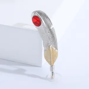 Détail d'une broche plume bicolore argent et or avec une pierre rouge sur fond blanc