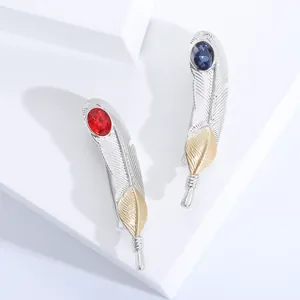Broche plume tendance avec pierres rouges et bleues sur socle géométrique blanc