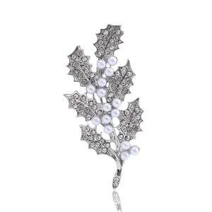 Broche feuille de houx argentée avec strass scintillants et perles blanches sur fond blanc
