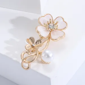 Detail view of gold shell clover brooch with pink enamel petals and pearl on a white stand