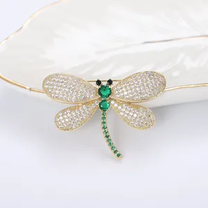 Exquisite gold dragonfly brooch with green gems and zircon wings on white texture