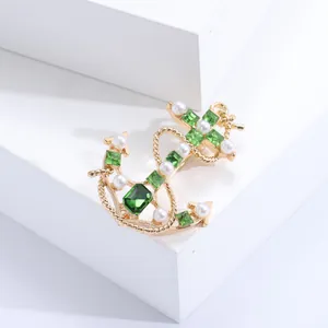 Navy style gold anchor brooch with green crystal and pearls on white background